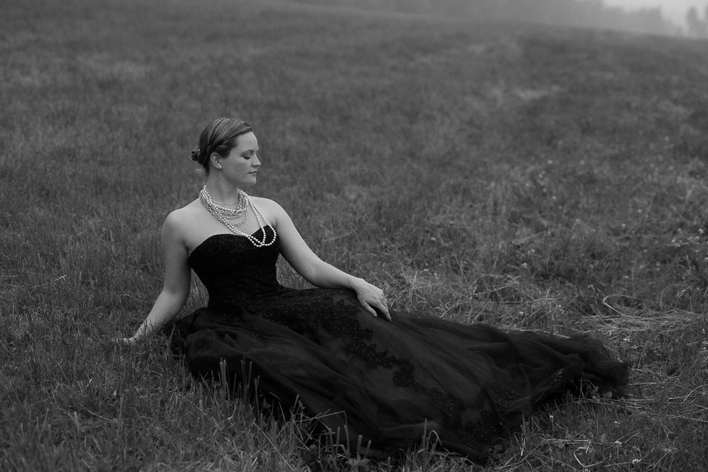 bride in a black wedding dress sitting in a field