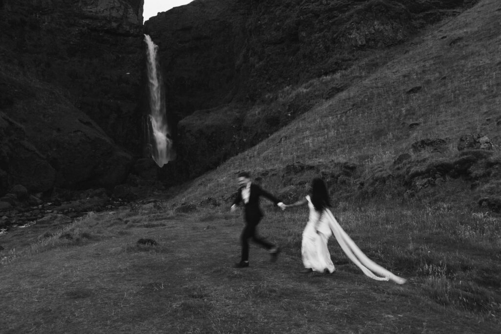 a couple running past a waterfall during their elopement. 