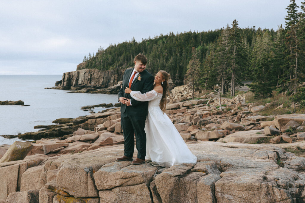 Couple holding each other in front of Otter Cliff in Acadia National Park