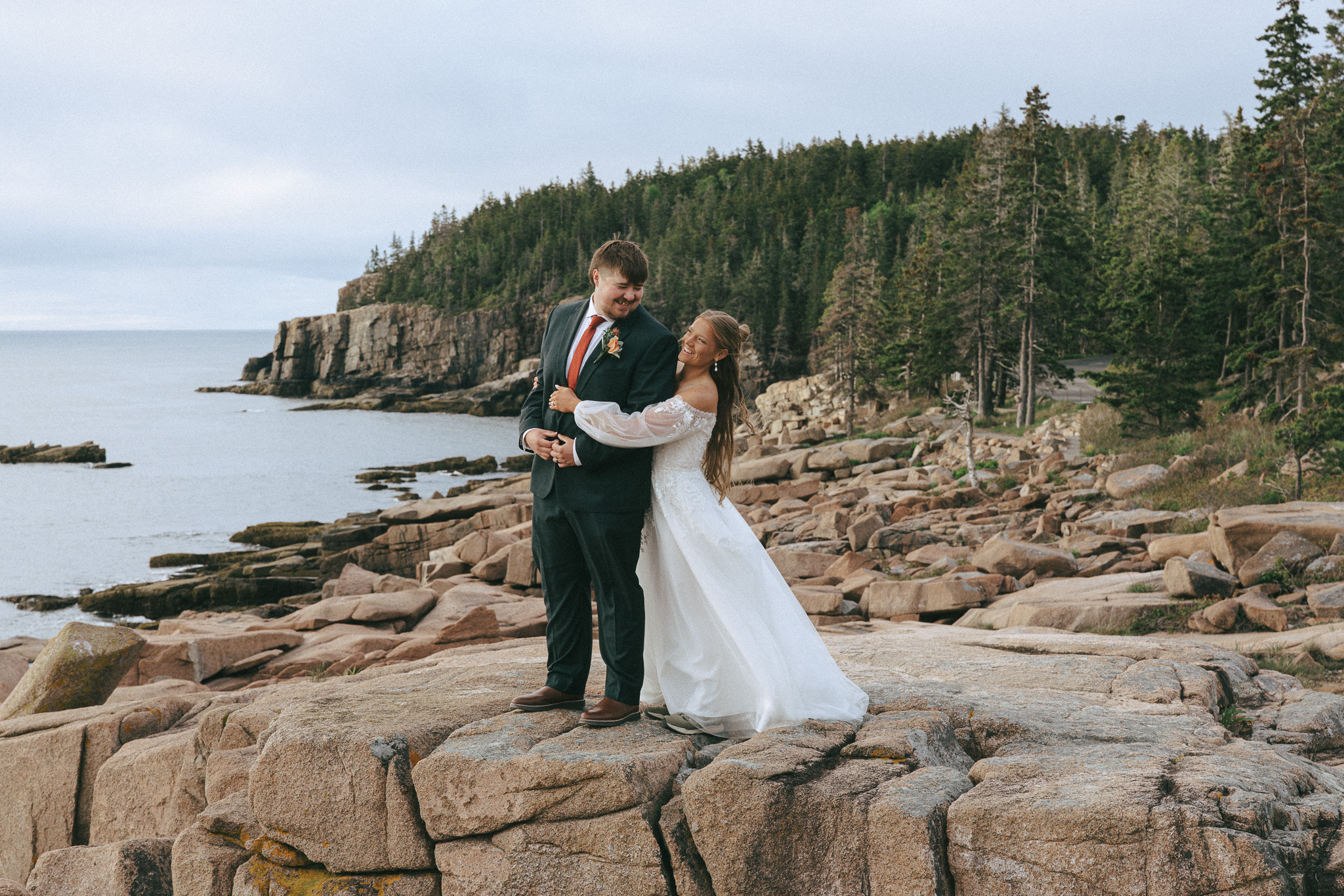 Couple holding each other in front of Otter Cliff in Acadia National Park
